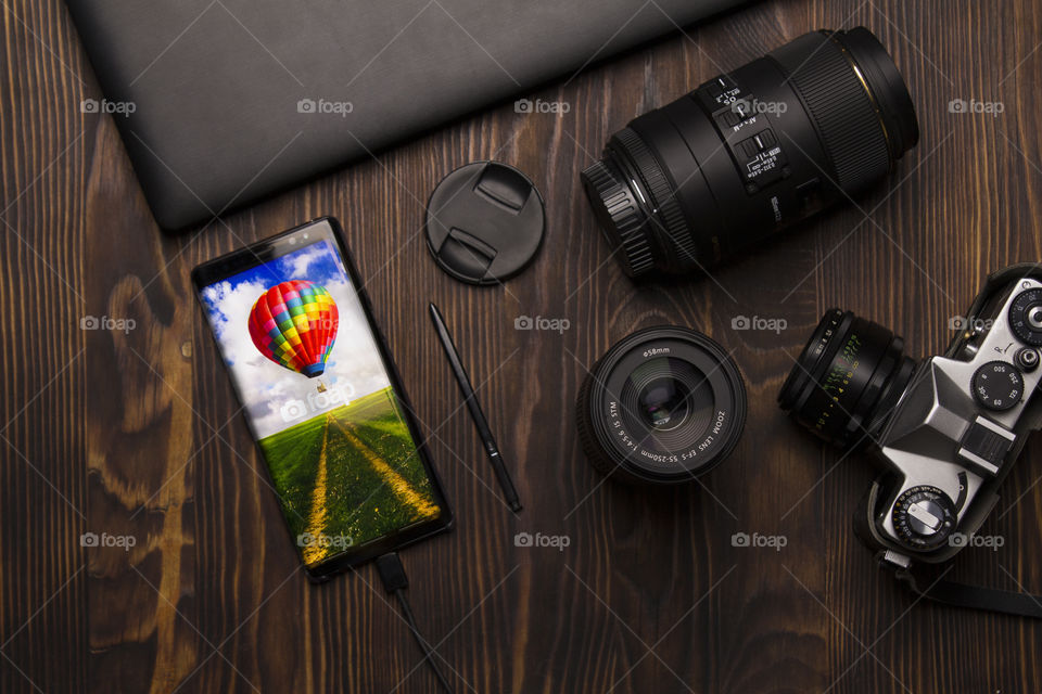 flatlay of modern smartphone,  lens and camera on a dark wood background.  welcome to Foap concept!