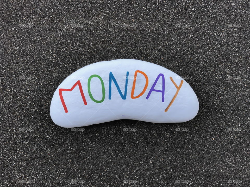 Monday, first day of the week carved and colored on a stone with black volcanic sand background