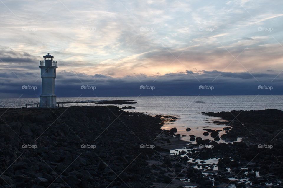 White lighthouse at an Icelandic beach during sunset.