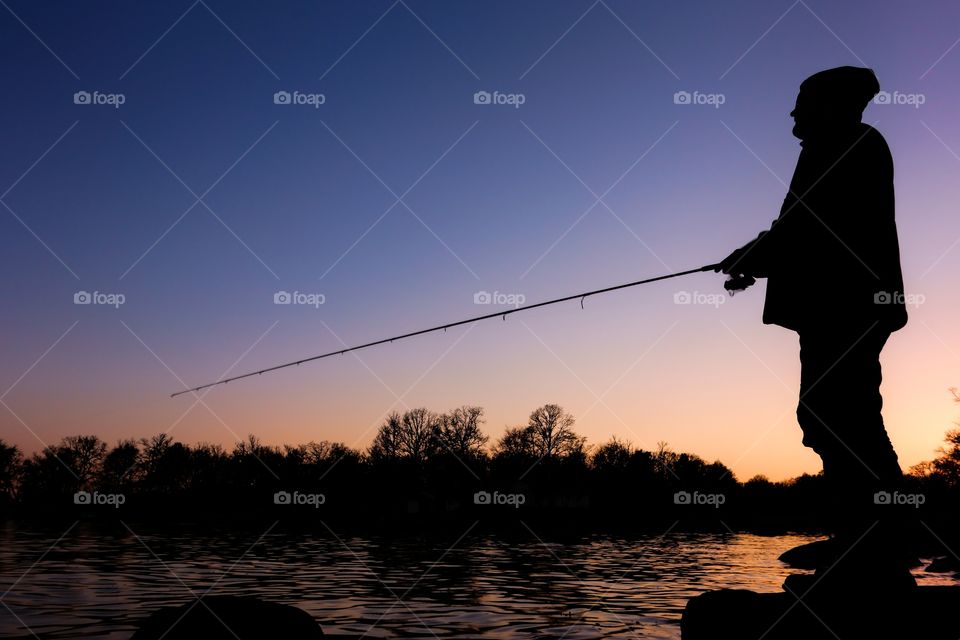 Silhoutte of a sportsfisheman standing on a rock and fishing on a bay in Blekinge Sweden at sunset time