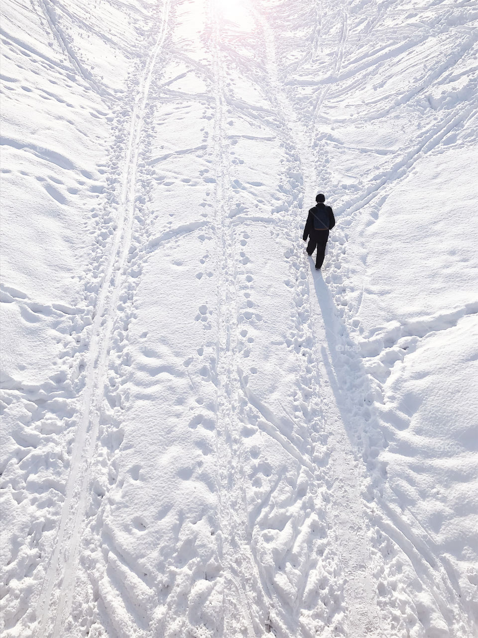 Man with a backpack walking by the white snow with lots of foot prints in winter 