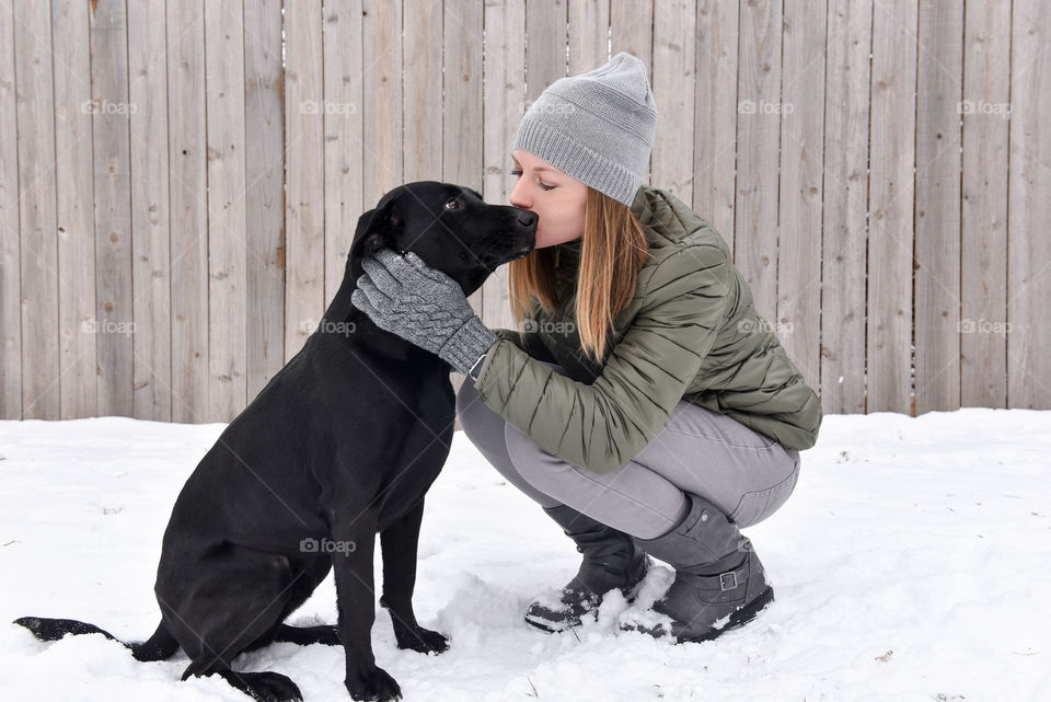 Young woman giving her pet dog a kiss outdoors in the snow