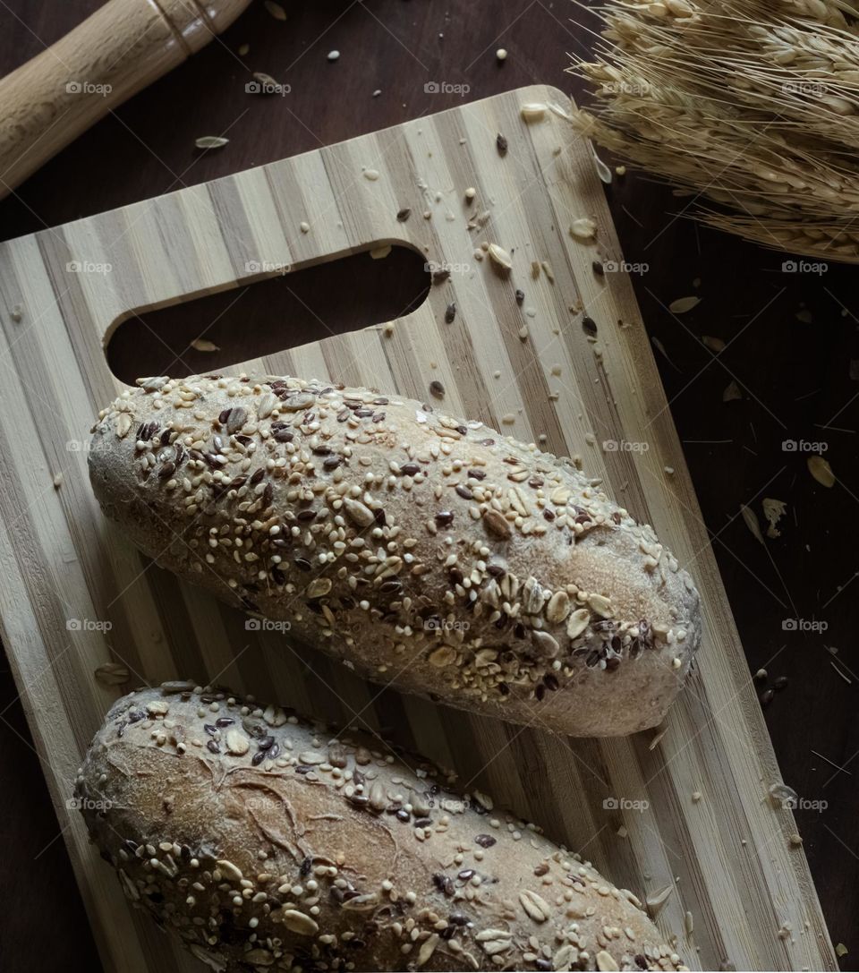 2 seeded rolls of a wooden board with knife and wheat