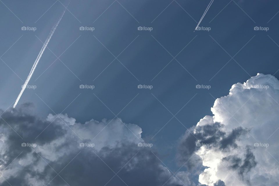 Sunbeams through storm clouds in the sky with contrails