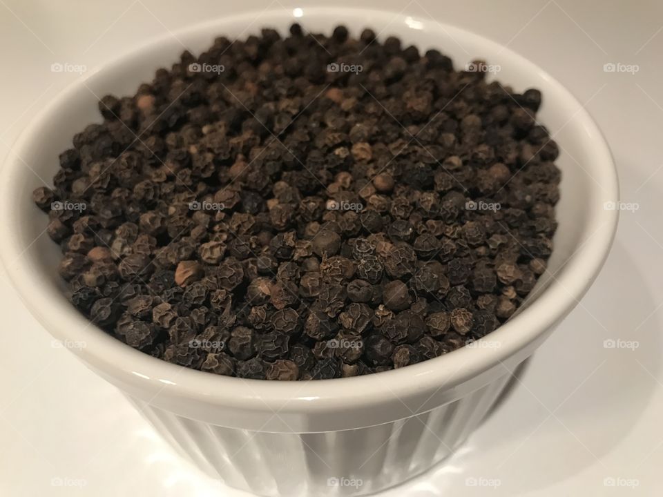 Black pepper in a bowl on white background 