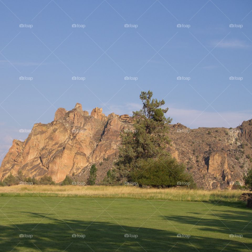 An evening golden glow sweeps down on a farm field leading to rugged South Rocks on a sunny summer day in Central Oregon.