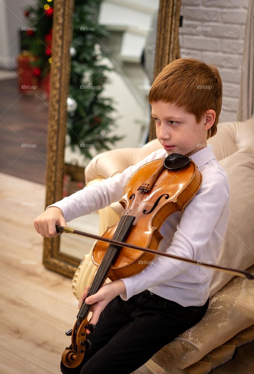 Red-haired boy plays the violin in a bright room