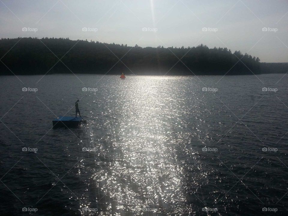 Person on floating dock on a lake. Sailboat in the background