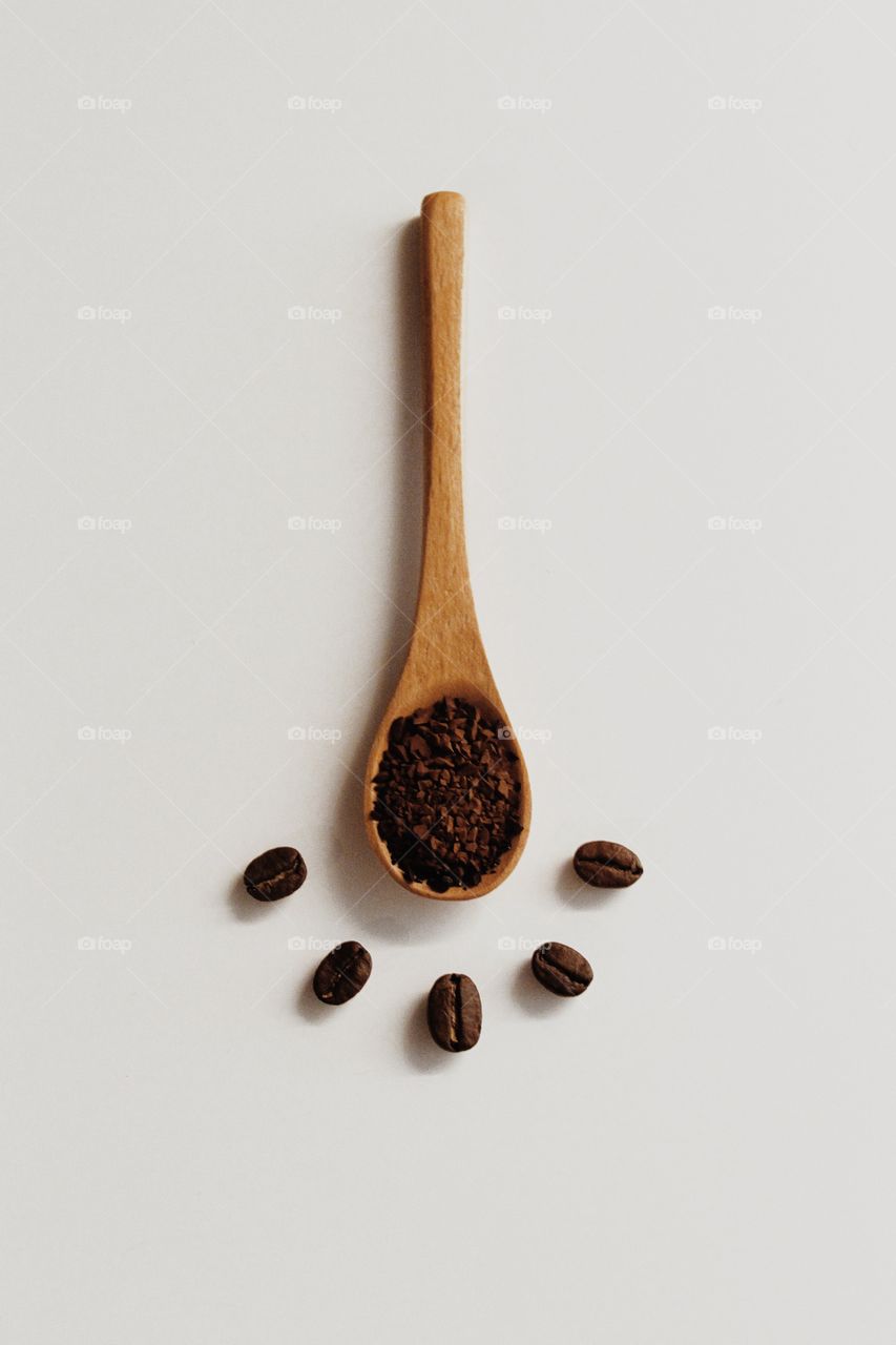 A spoonful of coffee powder with coffee beans