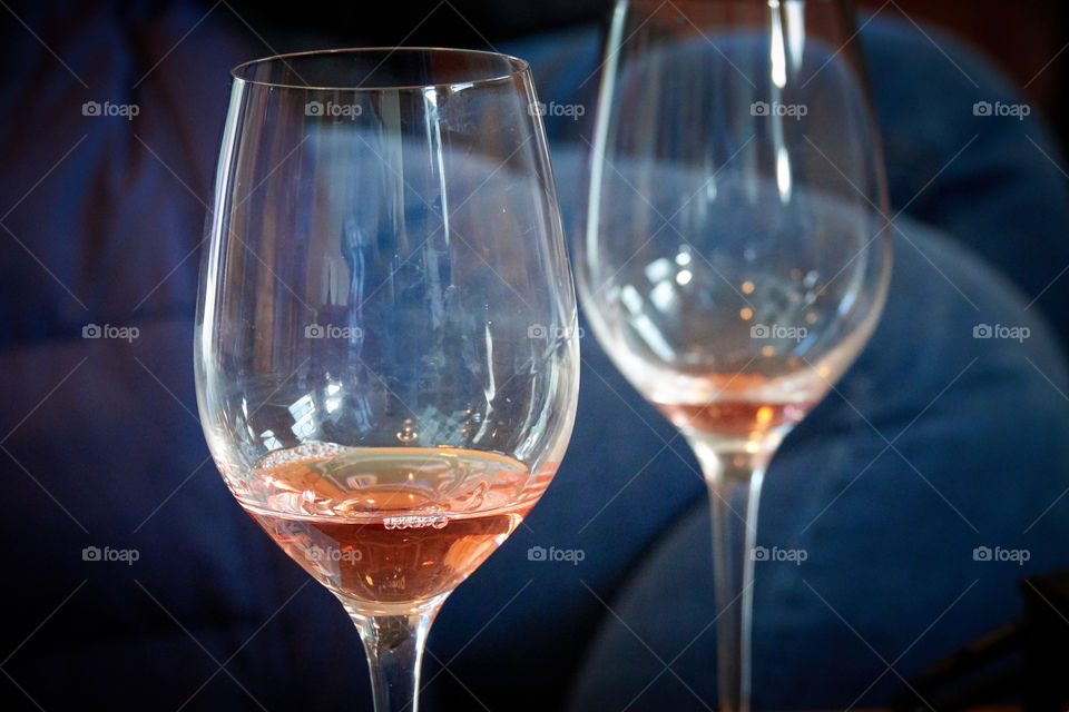 Two wine glasses, one in foreground, one in background, both with Rosé wine. A wine tasting at a winery. A pair of blurry denim jeans in the background indicating a casual affair with day-drinking.