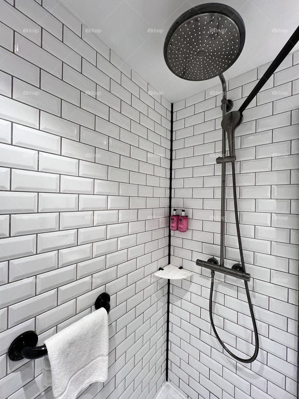 White bathroom with black shower and pink shampoo container 
