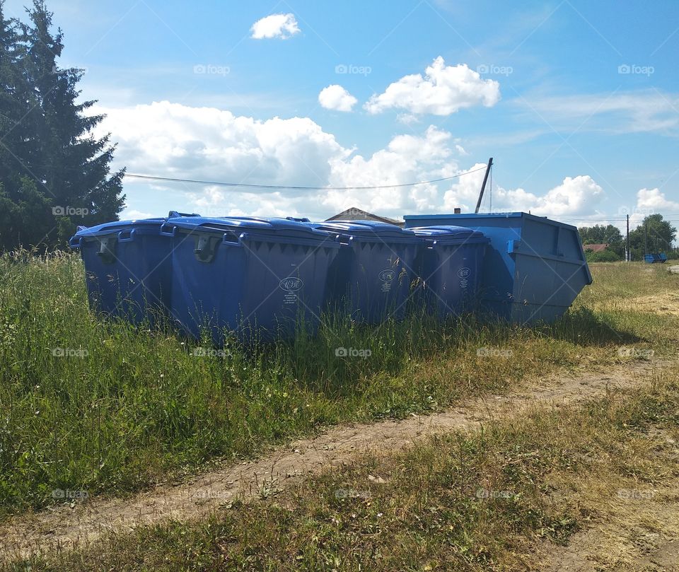 blue dumpster on green grass in a village under the summer sun