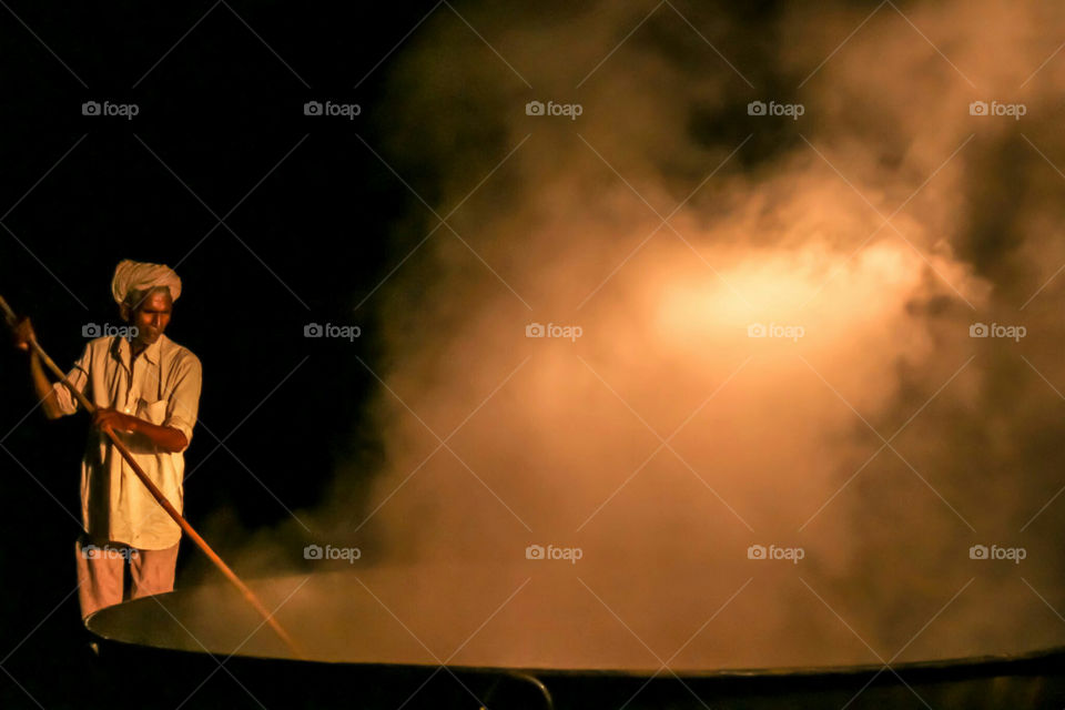 work. a person preparing jaggery by heating molasses from sugarcane in India