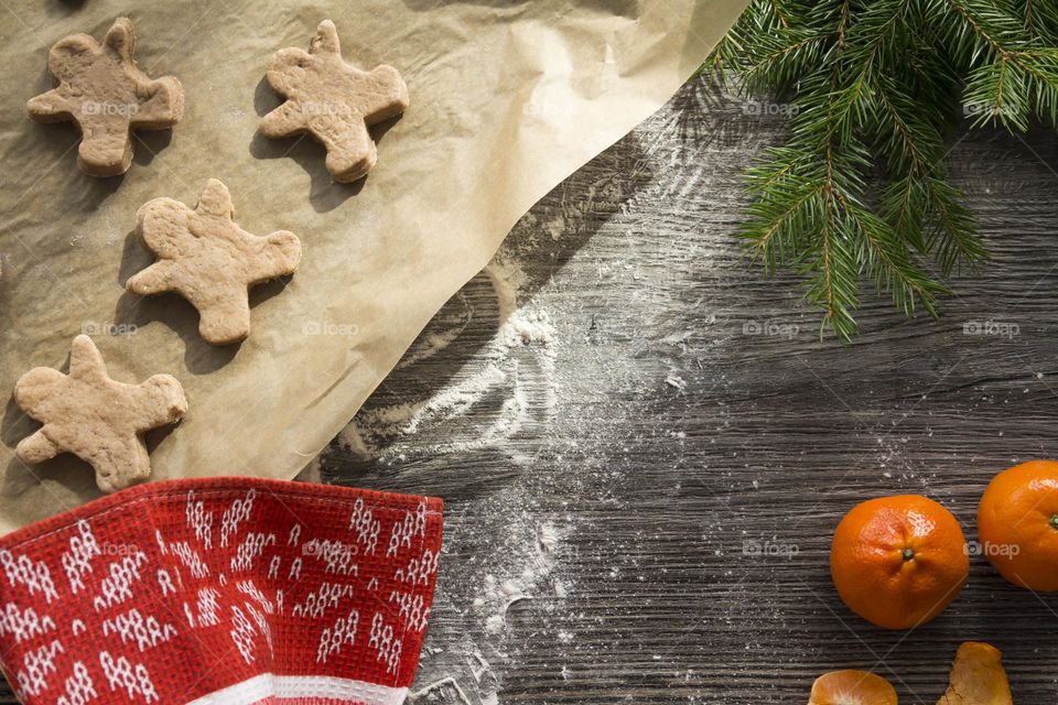 Cooking Christmas gingerbread cookies on a wooden table with tangerines and green Christmas trees.