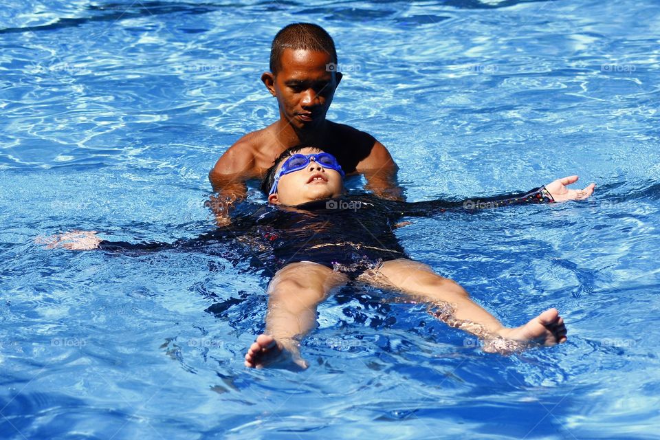young kid learns how to float on his back with the help of a swimming coach