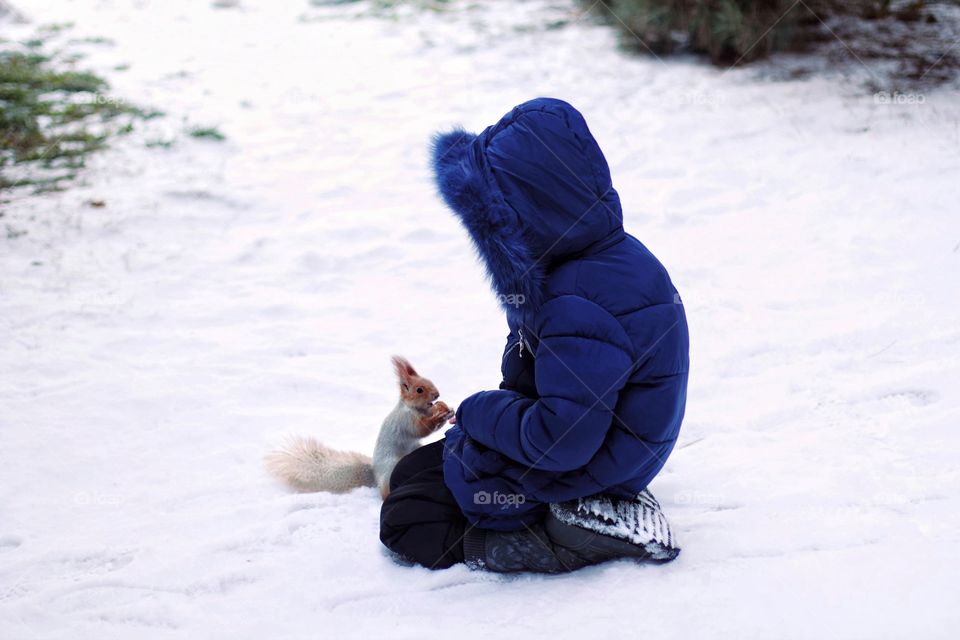 Little girl feeds a squirrel with nuts in the park