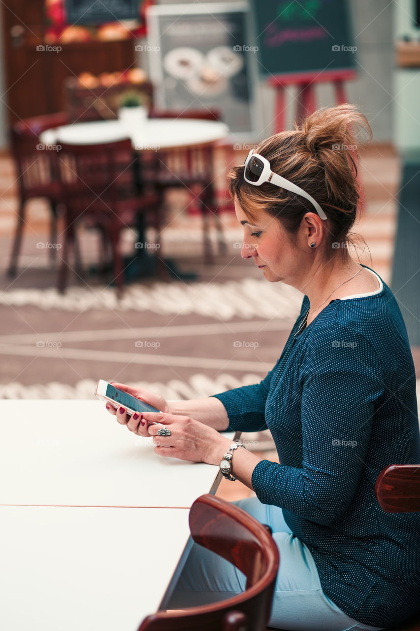 Young woman using mobile phone sitting by a table in cafe