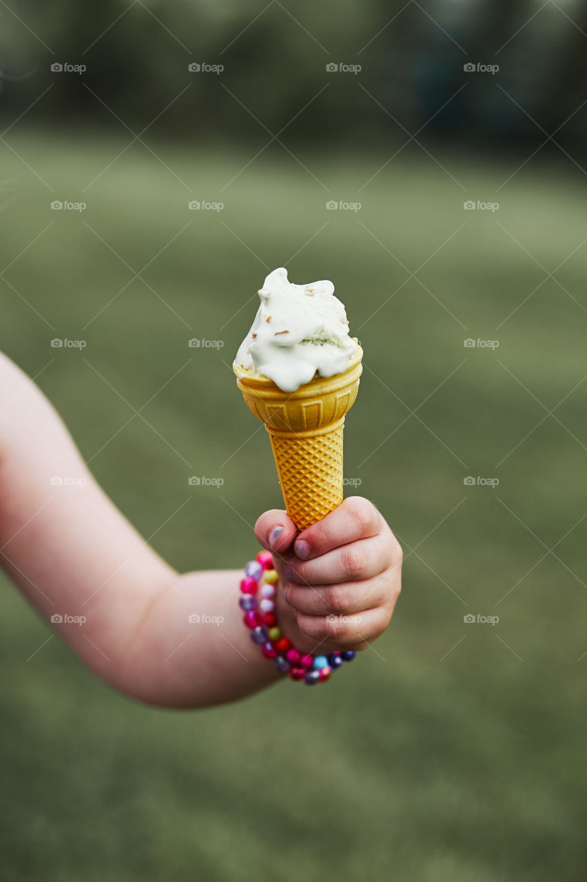 Close up of childs hand holding cone with ice cream over a plain natural green background. Candid people, real moments, authentic situations