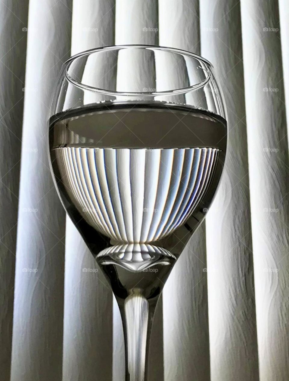 Still life of a wine glass half filled with water, against window blind