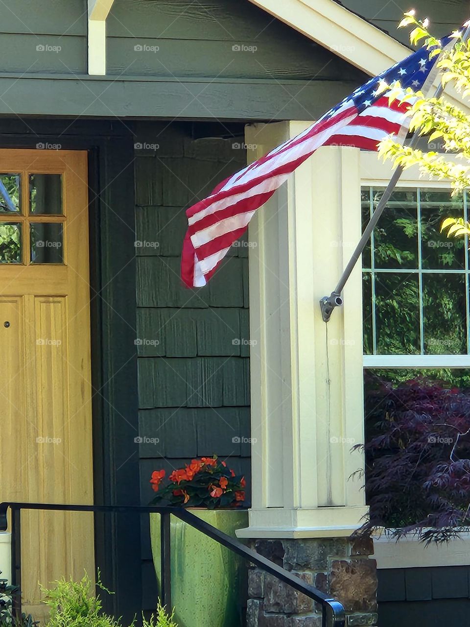 view of front door and porch of green house in Suburban Oregon neighborhood with American flag waving in the breeze