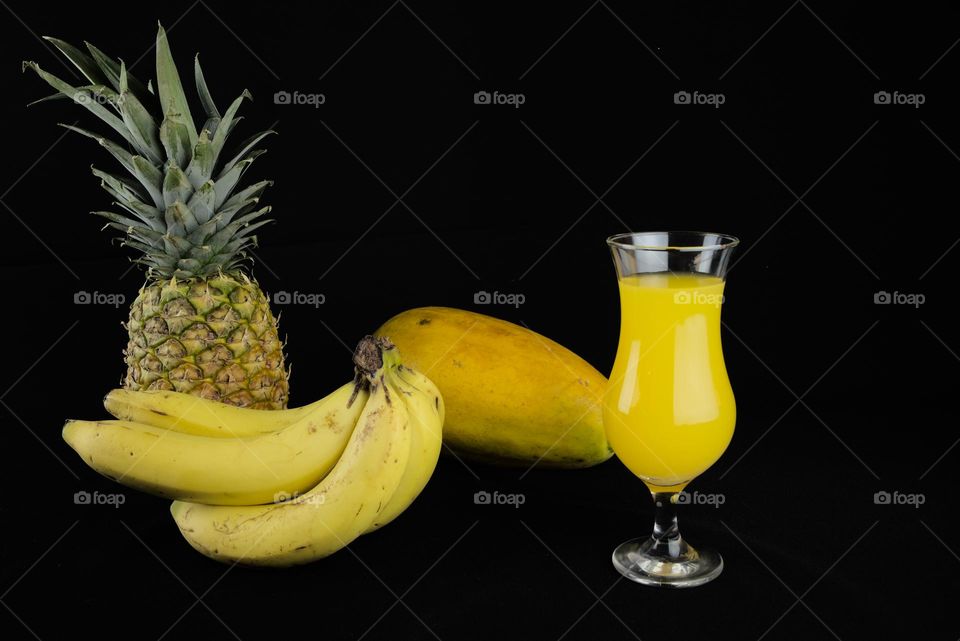 Tropical fruits and crystal glass with juice on a black background