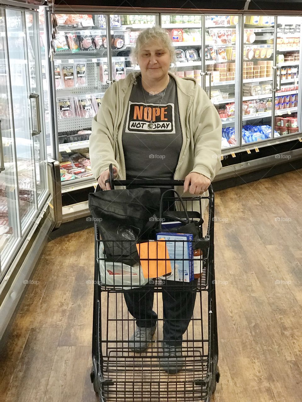 A woman shopping at the supermarket pushes her cart down a cold storage aisle. 