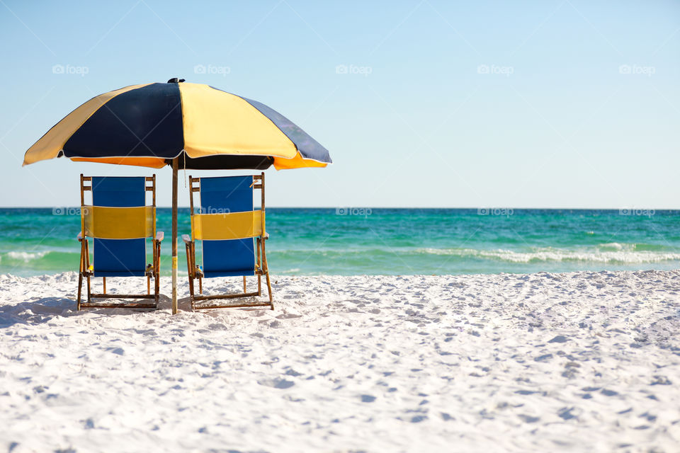 Beach chairs and umbrella sitting at a ocean front on sugar white sand in Florida
