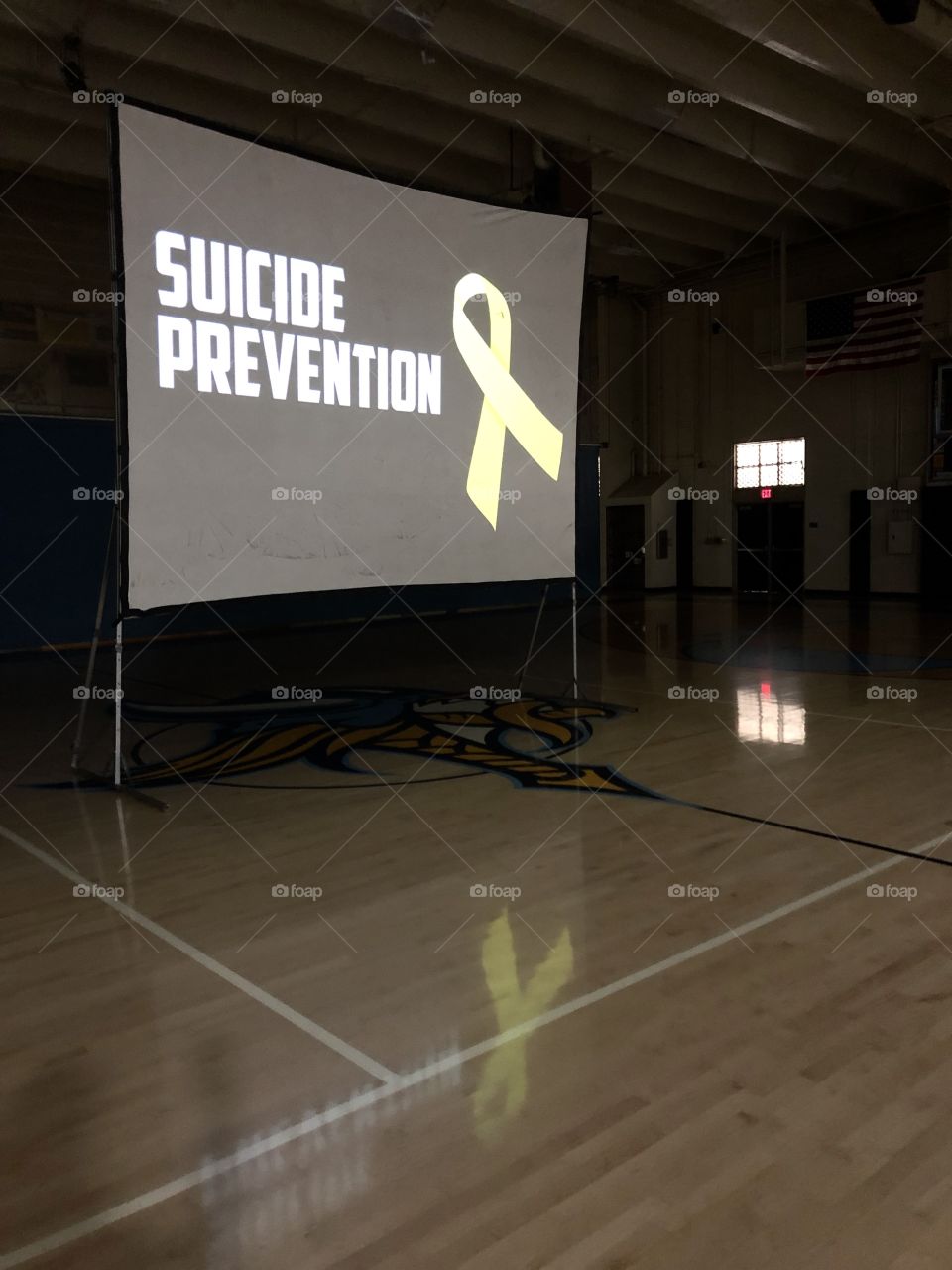 Suicide Prevention Week yellow ribbon assembly with projected presentation on large screen with reflection of yellow memorial ribbon on wood floor