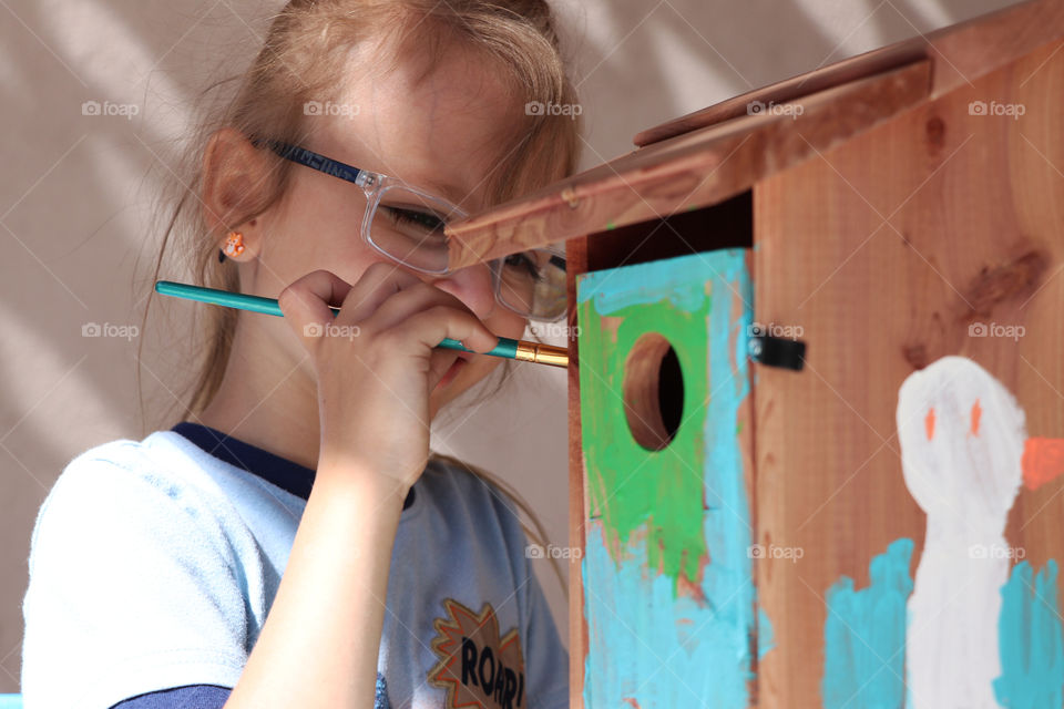 Child painting a wooden bird house