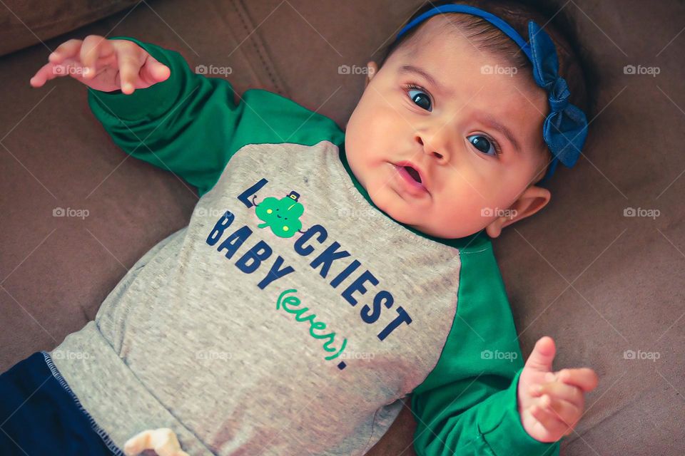 Baby with look of surprise while looking at camera, baby is surprised by mother, baby girl expressing surprise, cute baby is surprised, baby with St. Patrick’s Day gear on, luckiest baby ever t shirt on baby
