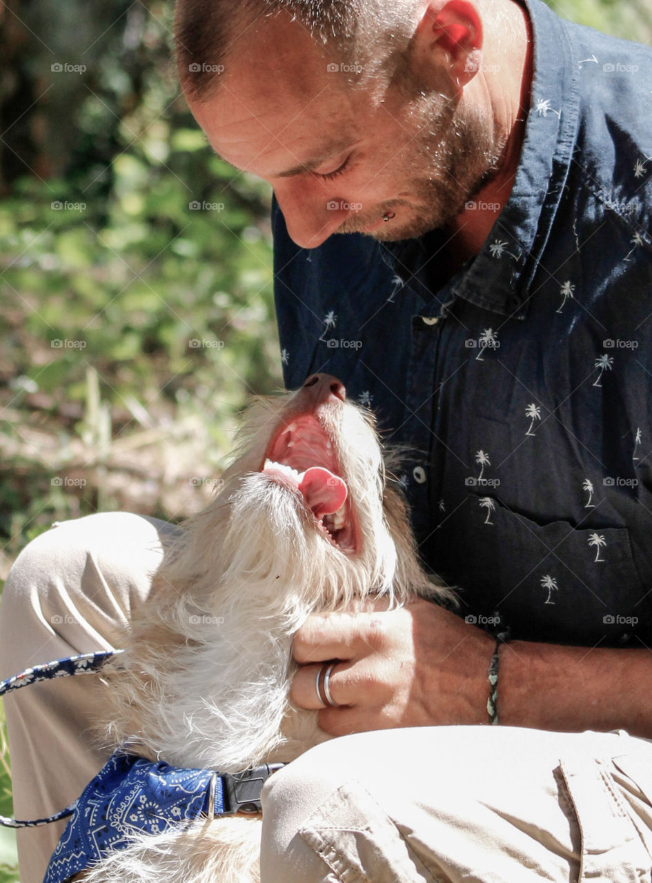 A puppy has her tongue hanging out as she looks adoringly at her owner, a middle aged man in a blue shirt