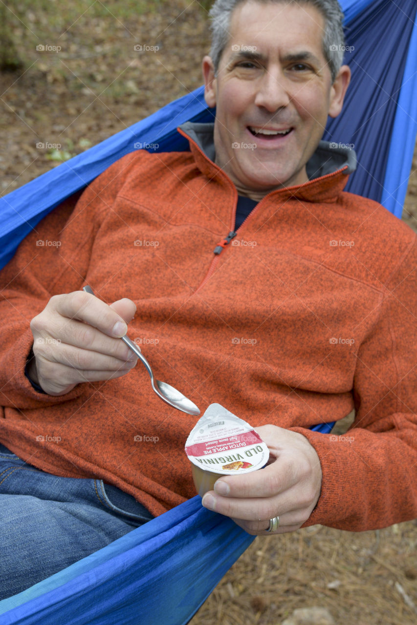 Smiling man enjoying a snack in a he hammock 