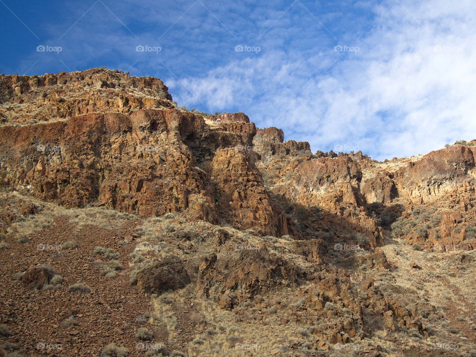 Rocky ledges and colored cliffs on hills with boulders and wild grasses off of the Crooked River Highway in Central Oregon on a sunny day. 
