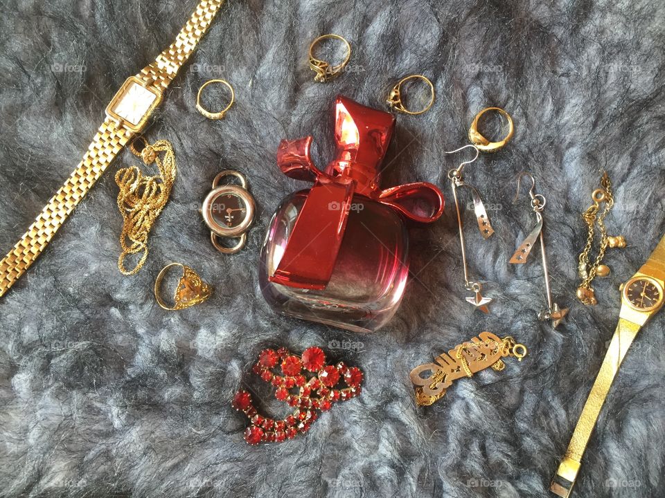 Red perfume bottle with golden watches and rings 
