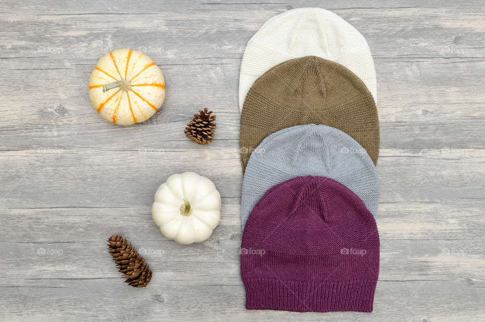 Flat lay of a row of knit beanie hats next to pumpkins and pinecones