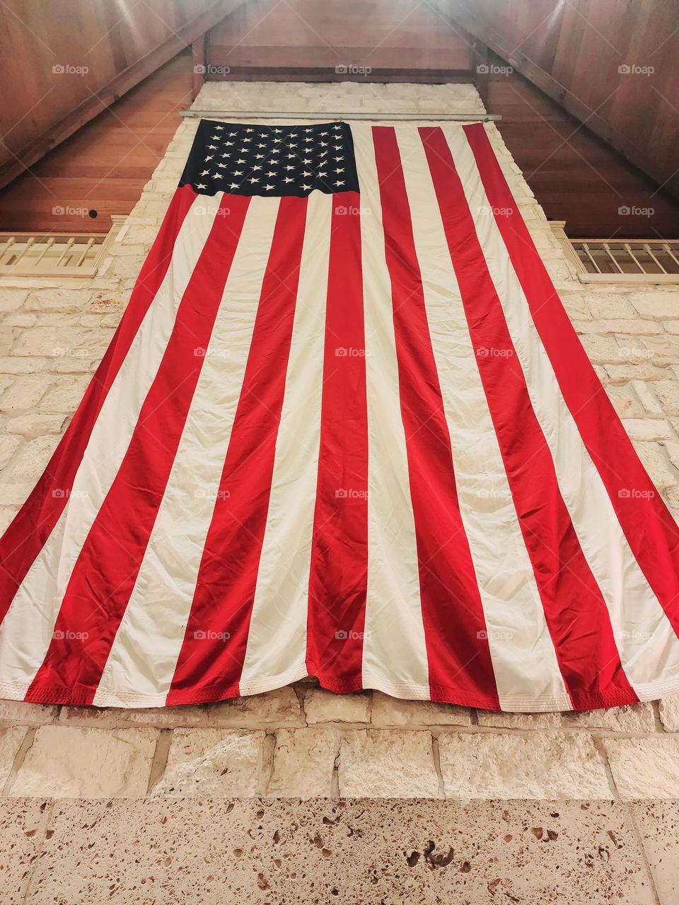 An American flag hangs on a wall constructed of white stone and warm wood
