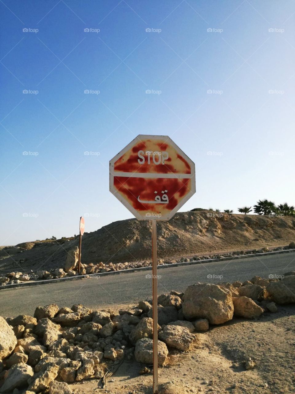 The red, old and funny arabic stop sign on desert road. With rocks arrangement.