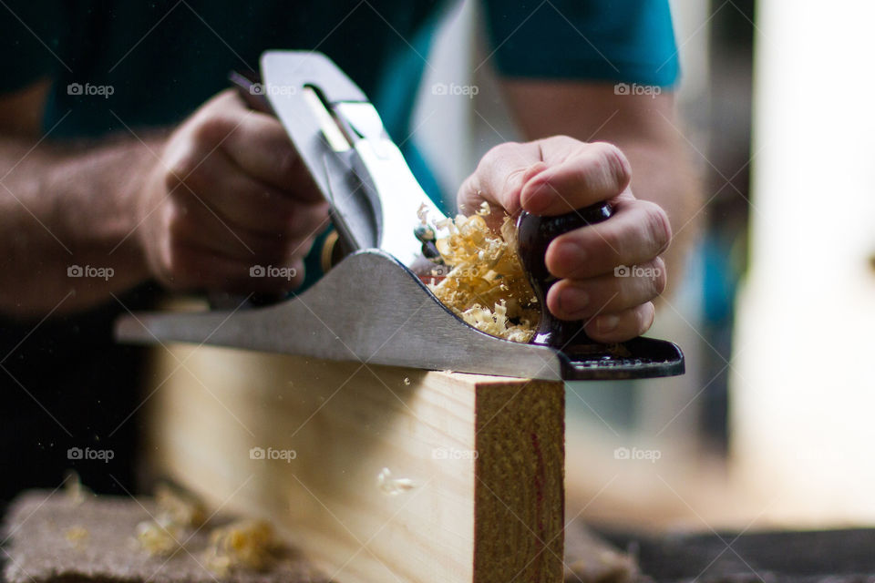 DIY at home - getting a chance to do things around the house! Image of man planing wood in preparation of making a table for home. Closeup of hands and wood shavings.