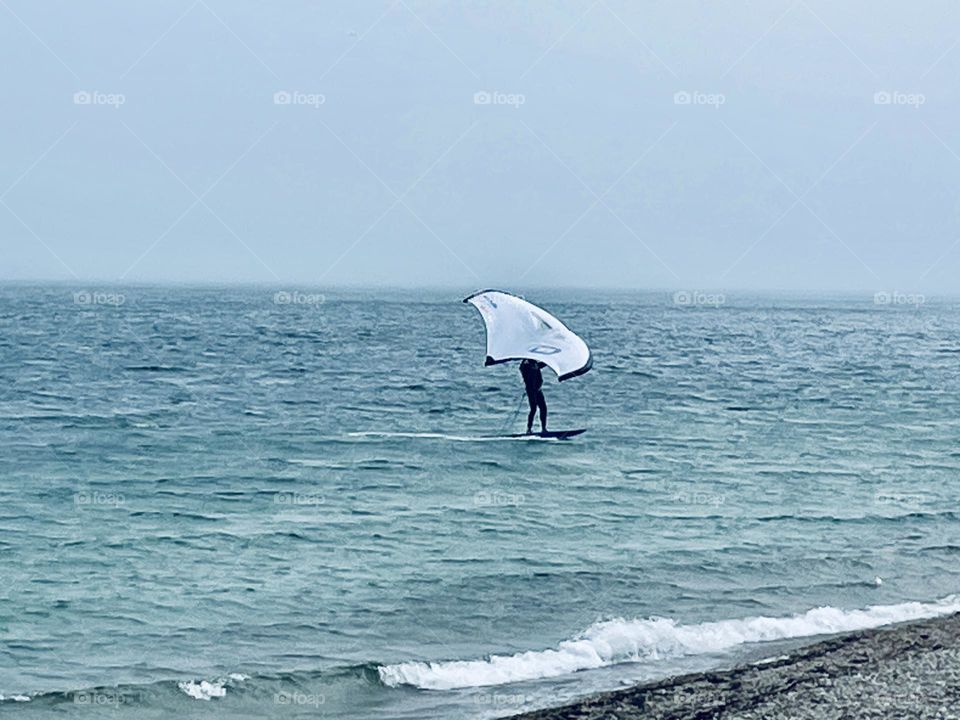 A man hydrofoil surfs above the Atlantic Ocean’s surface off Cape Cod on a breezy June afternoon, gliding smoothly as the foil lifts him above the gentle waves.