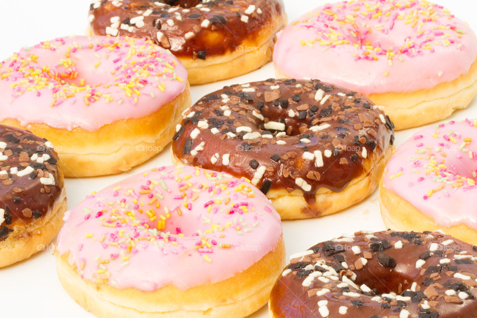 Rows of chocolate and pink iced donuts with sprinkles. Lots of doughnuts.