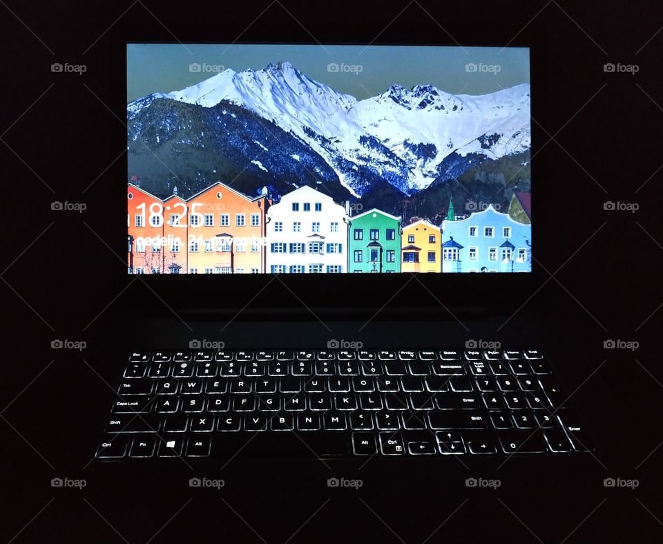 An indoor photo in the dark of a computer with white lights iluminated keyboard and colorful screen image