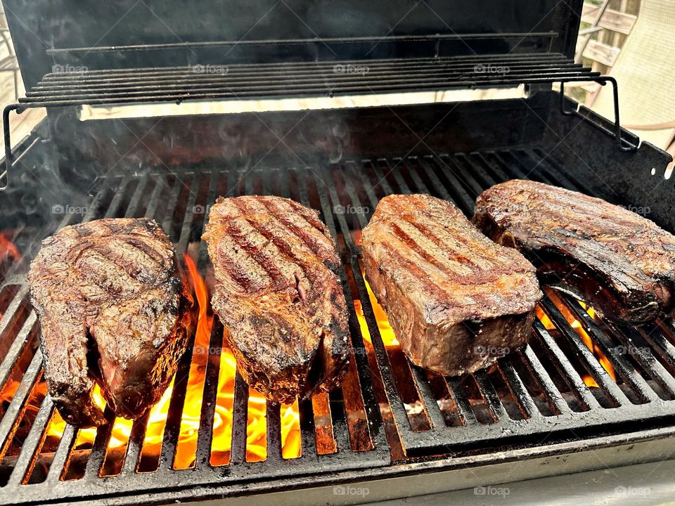 Summer cook out - The visible flames on a gas grill is being used provides direct heat for cooking the steaks. The grill marks are a result of the hot grates searing the meat, creating a crust and adding flavor.