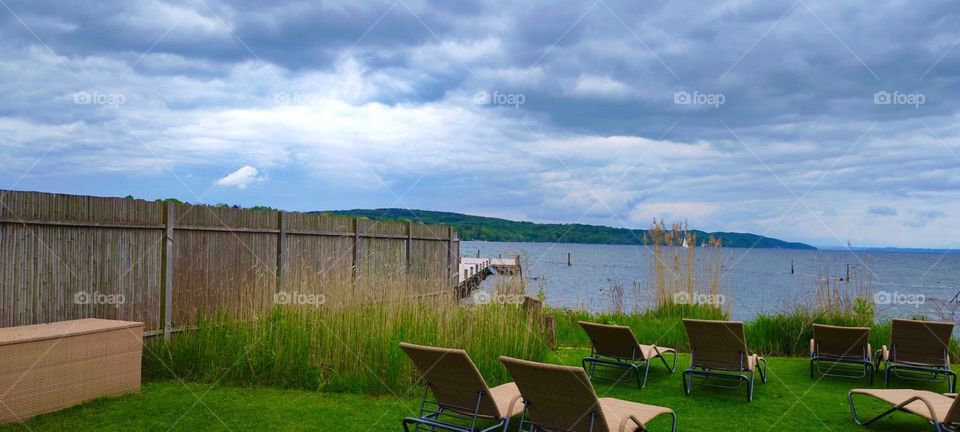 Lawn chairs are put up for sun bathers to use next to a large bamboo fence at the shore of the “Starnberger See”, a large freshwater lake in the vicinity of the small town of “Starnberg” in rural “Bavaria”. 2023. Hypnotic Productions