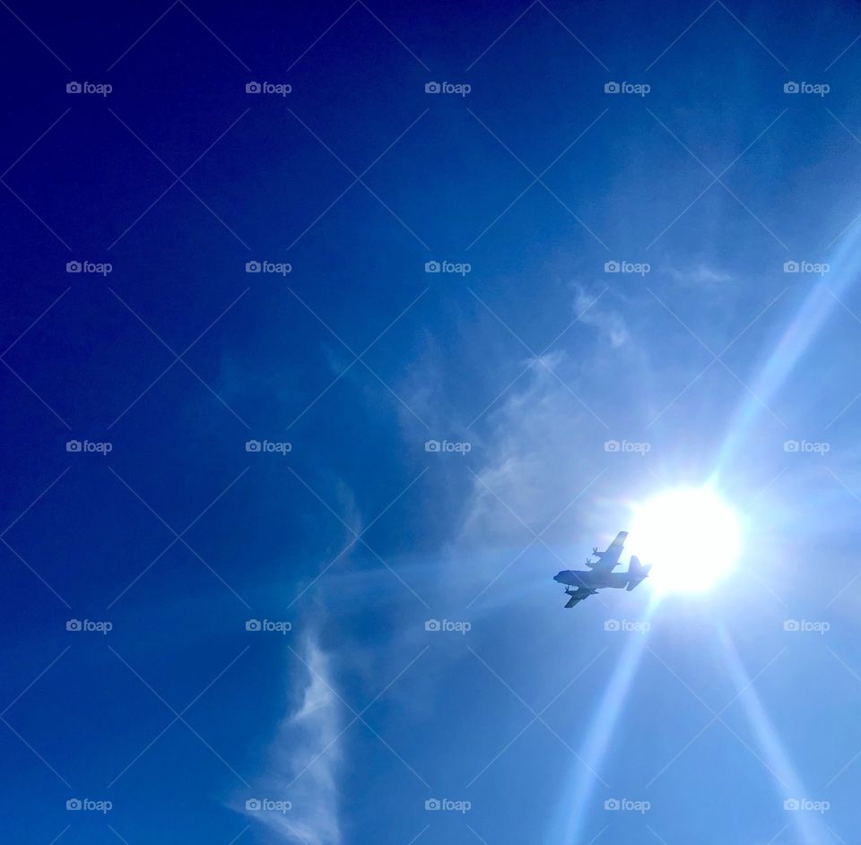Military transport plane passing directly overhead in front of sun and bright blue winter sky 