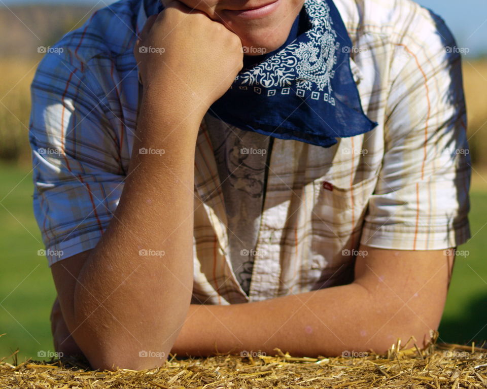 A young man poses on a haystack with the emphasis of the photo on his arms. 