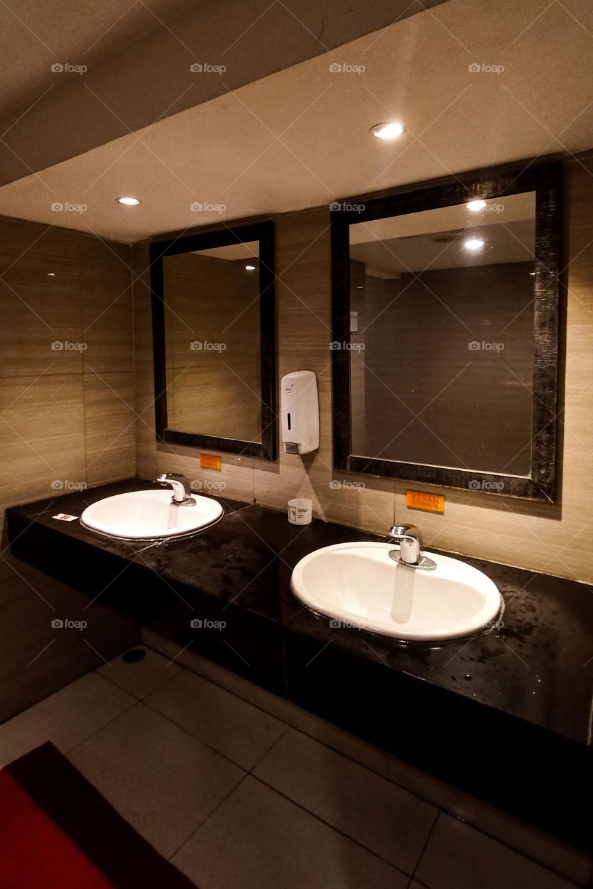 two white sinks with large mirrors above them in a warmly lit bathroom