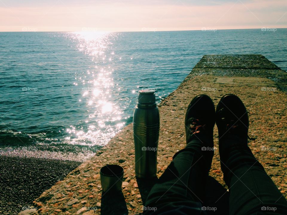 Feet at the morning sunrise at the sea with coffee 