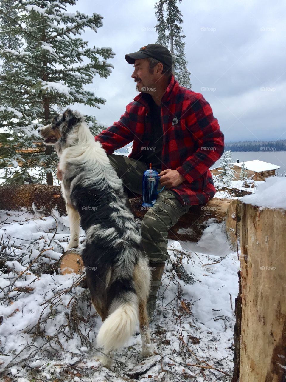 Mountain Man and his dog living Off Grid in the Canadian wilderness. Camo pants and buffalo jacket. 
