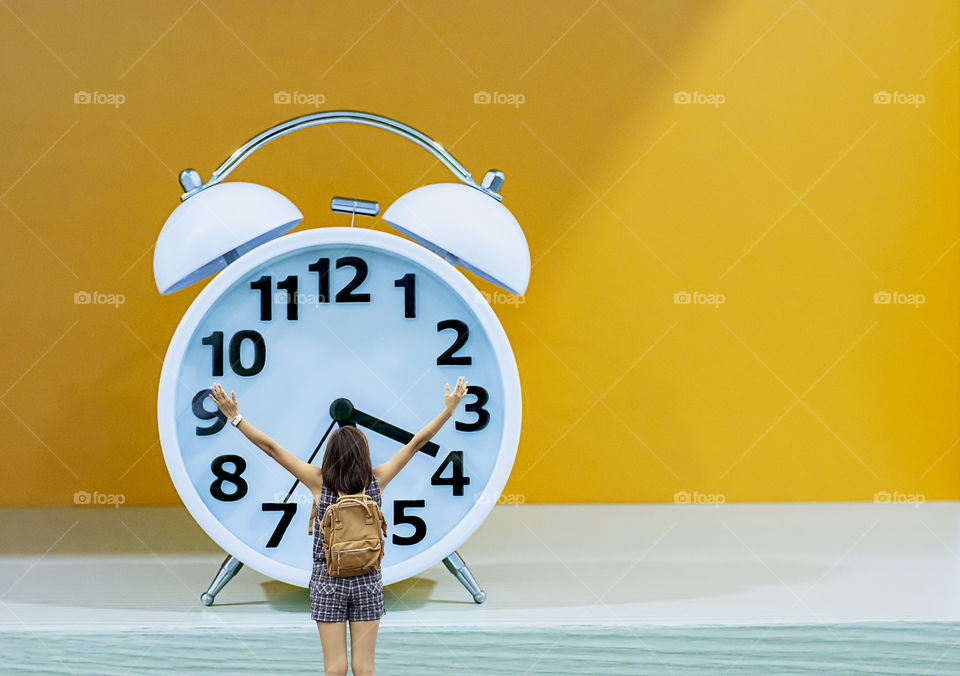 The image behind the woman raise their arms and shoulder backpack Background Alarm clock with a white and black dial on a orange background.