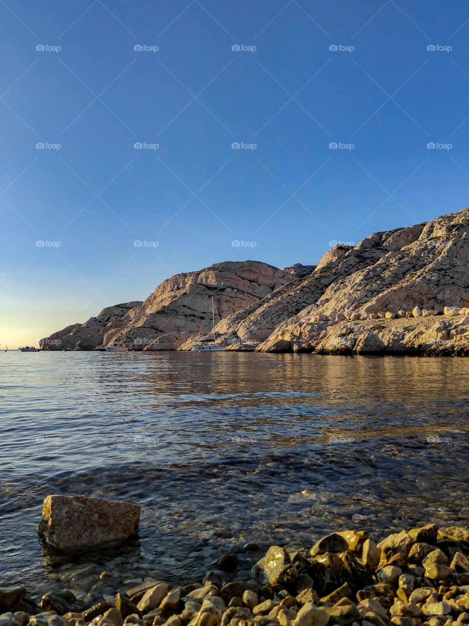 Beautiful calming wallpaper of the mediterranean sea, rocky pebble coast with sea water running on them with a view of the mountains on the island of frioul in France, close-up view from below.